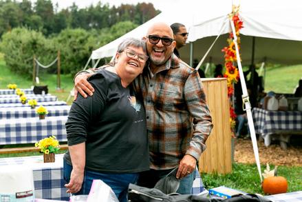 Two friends sharing a warm embrace at an outdoor event with picnic tables and tents