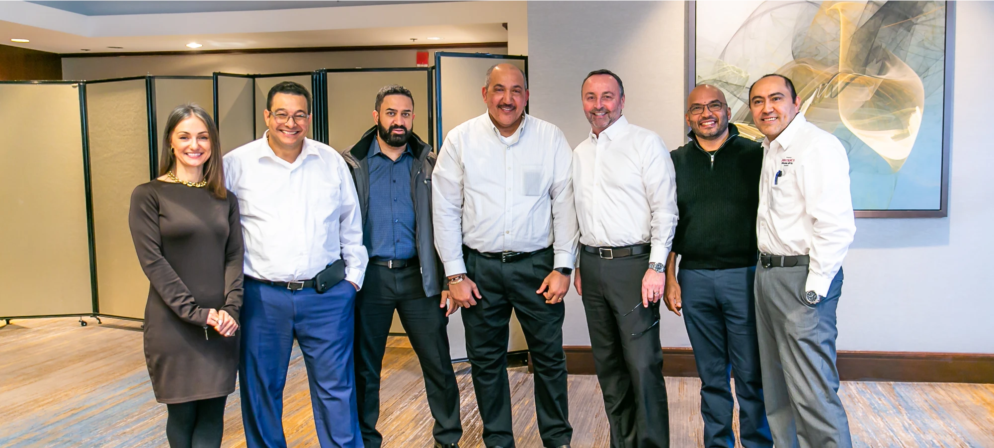 Smiling business team standing in a well-lit corporate setting with beige partition walls