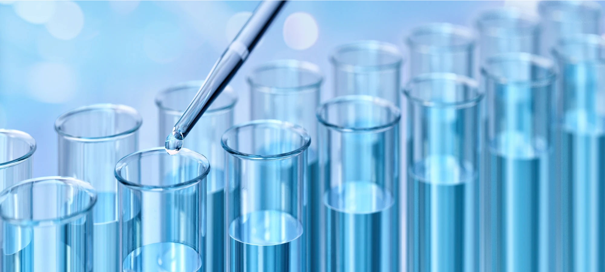 Close-up of a laboratory pipette dropping liquid into clear test tubes