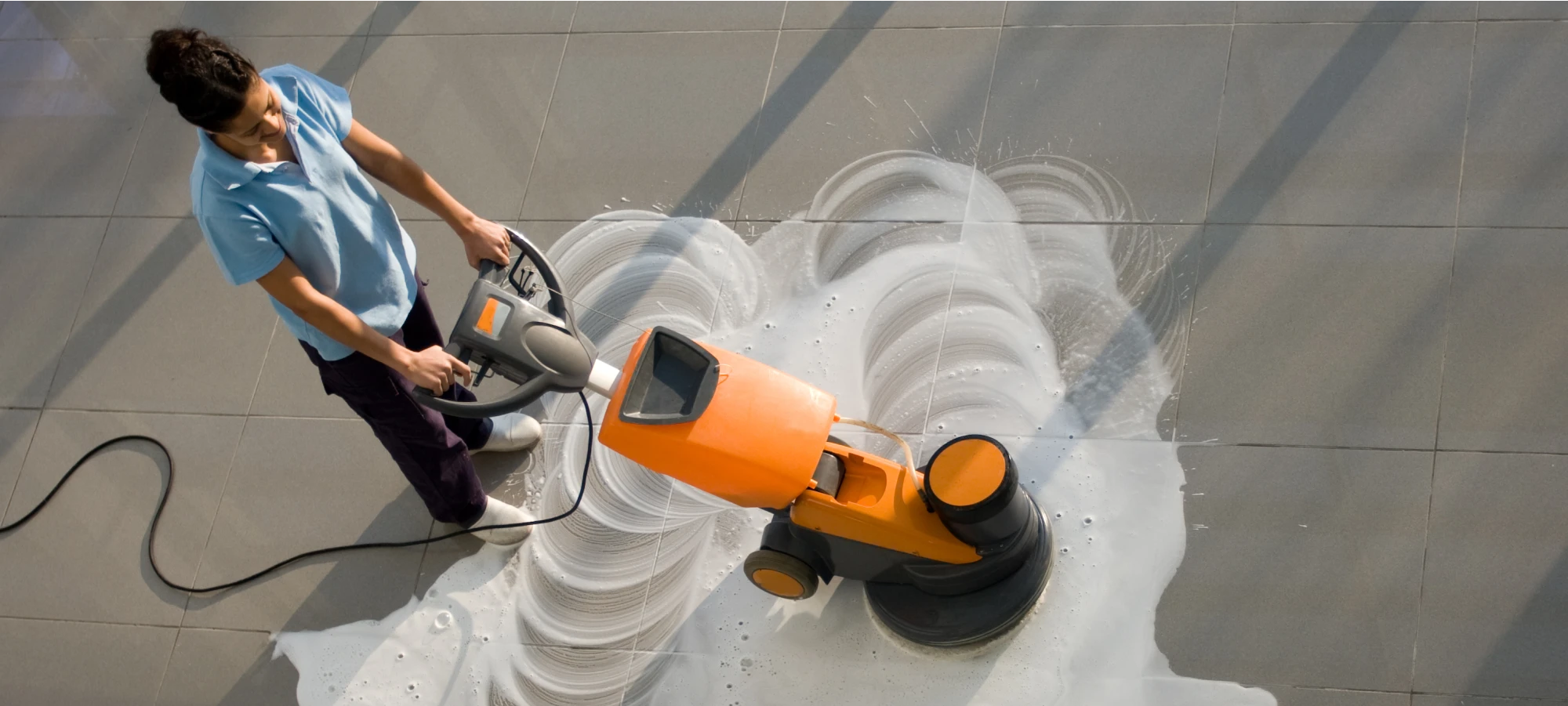 Janitorial worker using an industrial floor scrubber to clean large tiled surfaces