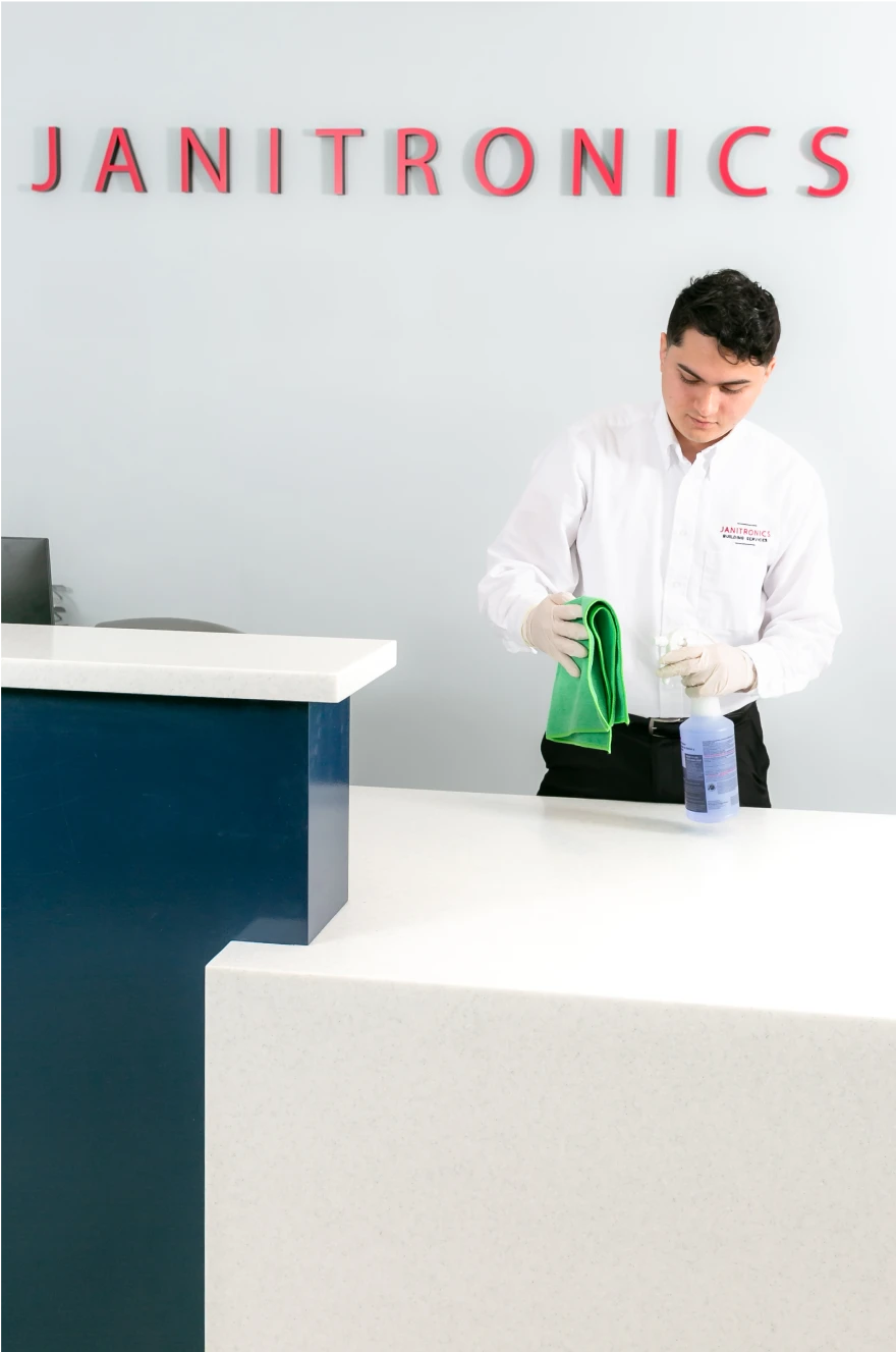 Office cleaner sanitizing a white reception desk at Janitronics Building Services