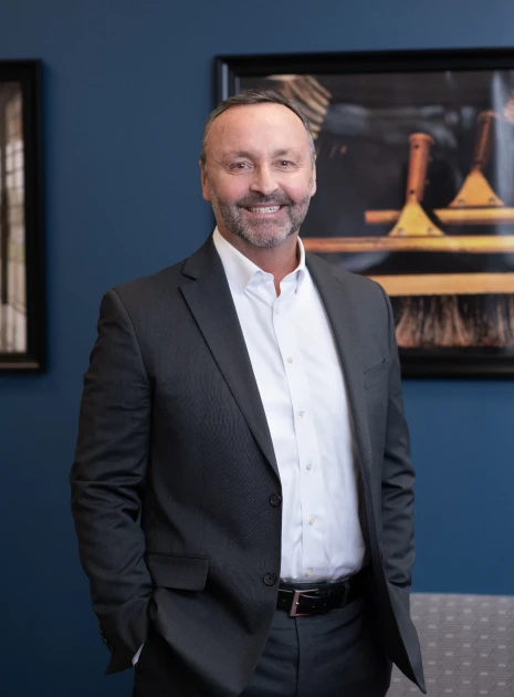 Smiling male executive in dark suit standing confidently against blue wall with framed artwork