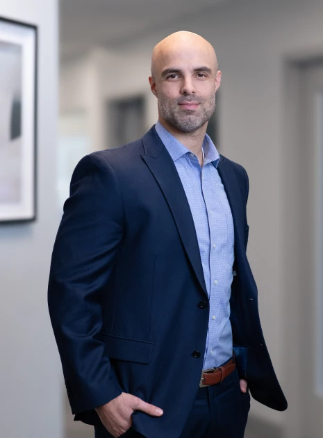 Confident executive in navy blue suit posing casually with hands in pockets in office hall.