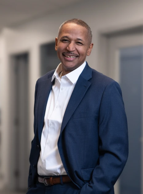 Portrait of friendly businessman dressed formally, standing relaxed with hands in pockets