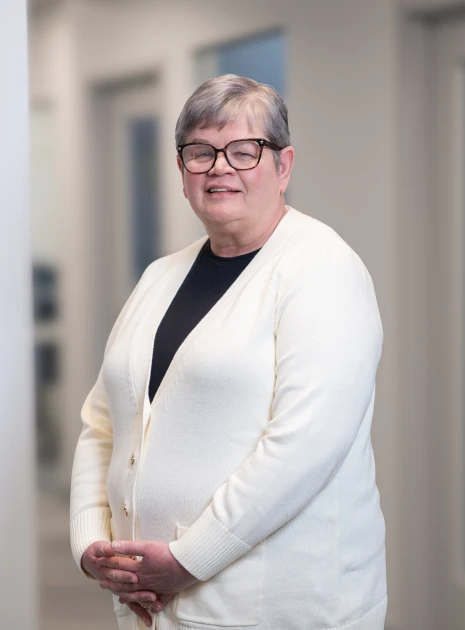 Senior team member dressed in cream sweater standing comfortably in workplace hallway