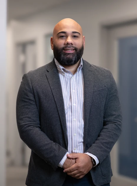 Friendly man in gray blazer and striped shirt smiling in office hallway setting