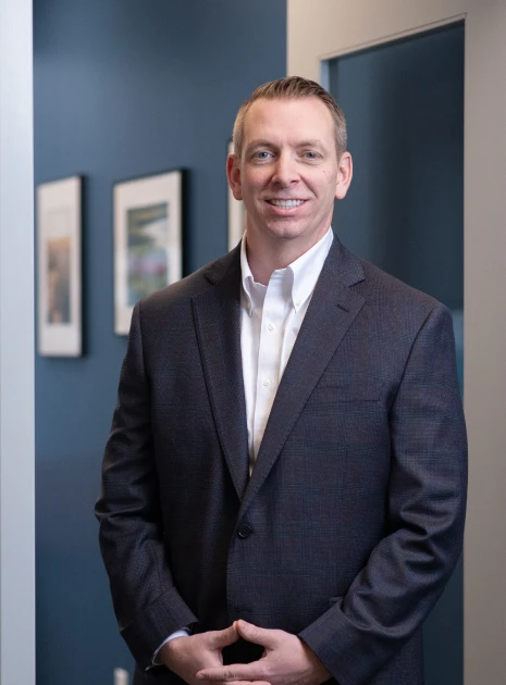 Confident male leader in slate blue suit and white shirt standing beside framed office artwork
