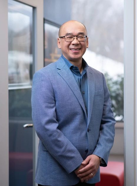 Professional man with glasses smiling confidently in modern setting with outdoor background