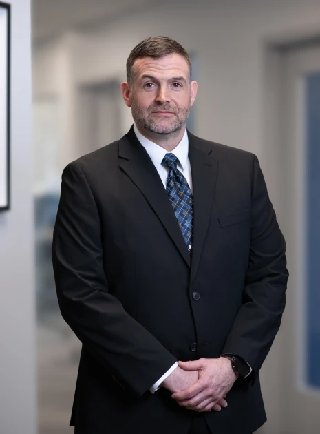 Businessman in black suit and blue patterned tie standing for professional portrait in hallway